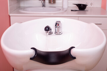 White washbowl with opened crane for washing hair in hairdressing salon