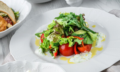 Fresh green salad with vegetables, tomatoes, arugula, spinach, lettuce, bell pepper, cucumbers and sauce on plate on light wooden background. Healthy food, clean eating, vegan, dieting, close up