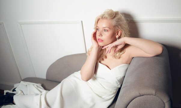 Bride on the sofa. Beautiful woman with short blond hair. A beautiful girl in a white wedding dress and silver earrings posing. Wedding photo .