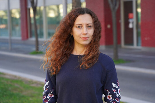 Portrait of a young woman with green eyes and curly red hair fluttering from the wind. The photo was taken on a street in Nice, France without a medical mask.