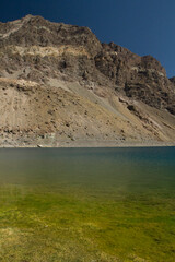 Natural background. View of the yellow shallows, blue water lake, rocky cliffs and mountains, high in the Andes cordillera in Chile.