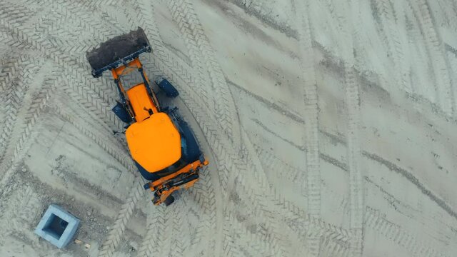 Backhoe loader works at a construction site, removing soil. Aerial top down view
