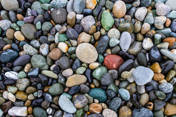 Colorful smooth rocks on the beach covered in water.