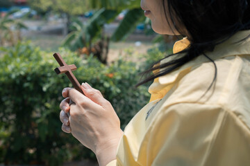 Asian woman praying with wooden cross outdoor.