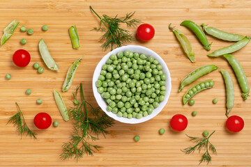 Fresh green peas in white bowl, red tomatoes, dill and pear pods on wooden background. Raw organic food mix. Fresh, healthy, vegan food concept. Flat lay photo.