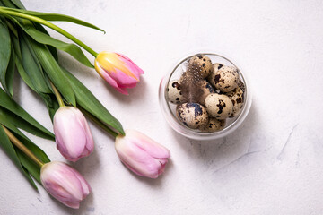 A bunch of brown quail eggs in a transparent bowl. Nearby are pink tulips. Preparing for Easter. Copy space, top view, flat lay.