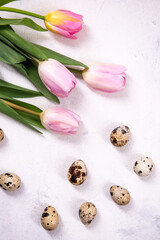 A brown quail eggs on a white background. Nearby are pink tulips. Preparing for Easter. Vertical oriented.