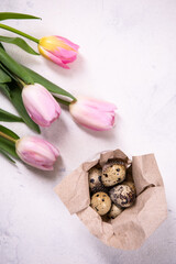 Close up. A bunch of brown quail eggs in a wrapping. Nearby are pink tulips. Copy space, top view, flat lay.
