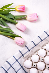 White chicken eggs in the tray, on a blue and white checkered napkin. Nearby are pink tulips. Top view, flat lay.