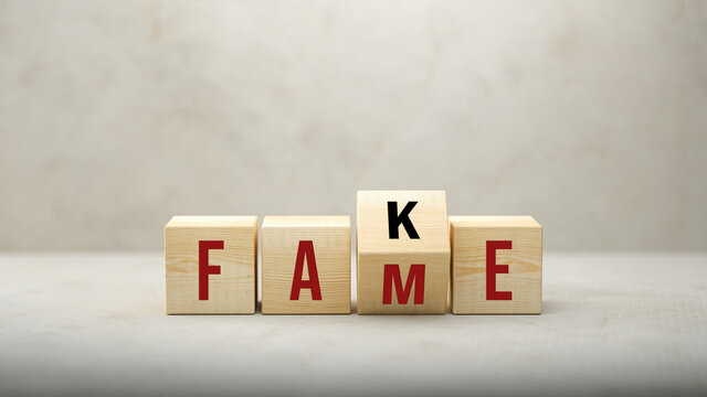 Fame or Fake concept with revolving letters on wooden cubes viewed low angle over a grey background with copyspace above
