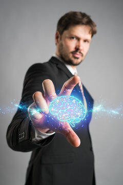 Businessman reaching forwards to grasp an AI icon of a shining blue brain emitting energy and power on a virtual interface or computer screen.