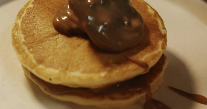 A tablespoon pours and spreads a cooked slide of pancakes with chocolate nutella mousse in slow motion