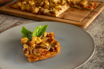 Pizza slice on a gray plate. Rectangular portion of homemade dough with chicken filling on top.