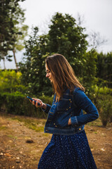 Young caucasian woman in blue dress and denim jacket with smartphone. 