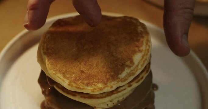 Chef's hand adding fourth pancake uphill with chocolate cream in slow motion