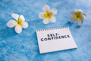 positive attitude concept, Self-confidence text on notepad with tropical flowers around it
