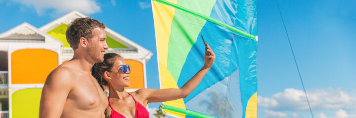 Happy summer couple taking selfie on Florida beach on travel vacation. Sunbathing woman in bikini using phone with man friend. Panoramic banner. - obrazy, fototapety, plakaty
