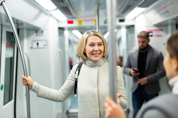 Fototapeta na wymiar Portrait of mature woman talking friendly with her fellow traveler in modern subway car..