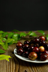 Jabuticaba fruit in a bowl and a black and wooden background with jabuticaba leaves. Brazilian typical fruit