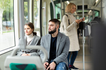 Fototapeta na wymiar Young stylish brunette and bearded guy traveling by modern city bus, looking out window in autumn day