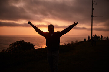 Fototapeta premium Hombre joven feliz levanta los brazos durante un atardecer de verano. Hombre mirando al horizonte del mar. 