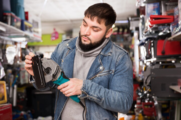 Attentive bearded man choosing jigsaw in hardware store