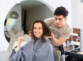 Obraz premium Young woman at beauty salon choosing hair treatment with male hairdresser