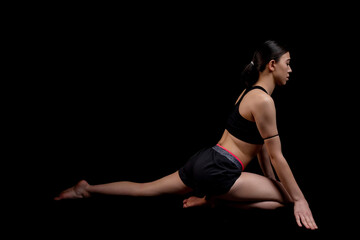 Young woman doing fitness exercise training isolated on the black background. Horizontal shot.