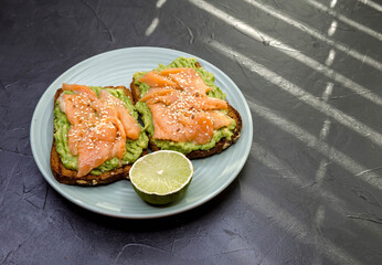 Open sandwich with dark rye bread, avocado and salmon. Homemade toast on gray concrete background. Black background, top view, free space. Healthy protein food, breakfast, lunch concept. Gourmet snack