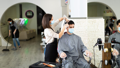 Portrait of female hairdresser and male client wearing protective masks and gloves during haircut at local hair studio