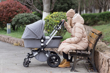 Happy Mother walking With Stroller In Park. Joy of motherhood. Stylish young caucasian woman wearing warm clothes at autumn.
