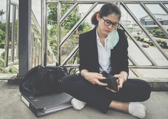 Asian unemployed businesswoman sitting on footbridge, stressed after laid off from work because impact from covid-19 pandemic outbreak.