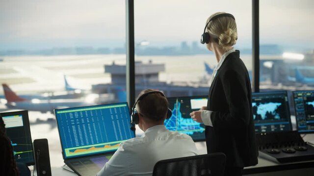 Female and Male Air Traffic Controllers with Headsets Talk in Airport Tower. Office Room is Full of Desktop Computer Displays with Navigation Screens, Airplane Departure and Arrival Data for the Team.