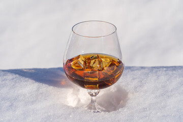 Glass of cognac with ice on a bed of snow and white background, close up