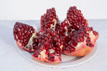 Open pomegranate fruit with red seeds on a white snow in winter, close up