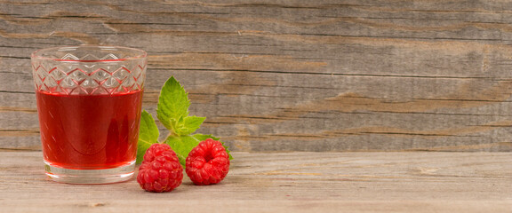 homemade sweet raspberry wine or juice in small glasses with fresh berries on aged wooden table