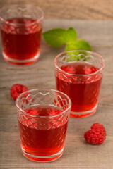homemade sweet raspberry wine or juice in small glasses with fresh berries on aged wooden table