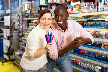 Glad positive smiling African man and European woman choosing pens and pencils in office supply shop