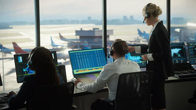 Female and Male Air Traffic Controllers with Headsets Talk in Airport Tower. Office Room is Full of Desktop Computer Displays with Navigation Screens, Airplane Departure and Arrival Data for the Team.