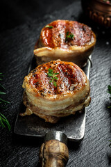 Medallions steaks from the beef tenderloin covered bacon on old meat butcher on Dark background. Top view vertical image