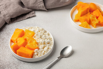 Healthy breakfast. Cottage cheese with pieces of baked pumpkin in orange sauce in a plate on the table.