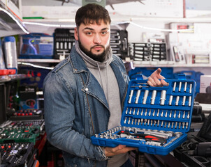 portrait of young serious male is standing with new ratchet in tools store
