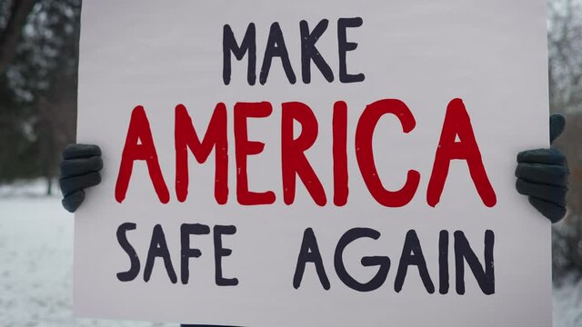 Man holding a white sign while standing in the park. Make America Safe Again Announcement. Man participates protest, calling on the government to stop the war, reform the social and economic system