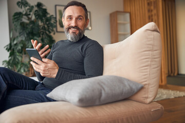 Fototapeta premium Caucasian adult man is sitting with smartpone in modern cozy office lounge zone