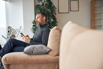 Obraz premium Caucasian adult man is sitting with smartpone in modern cozy office lounge zone