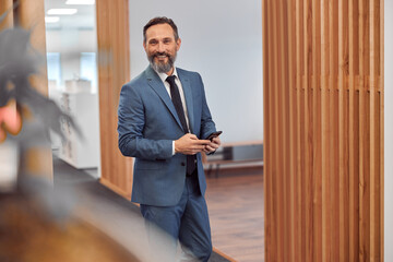 Happy adult caucasian businessman using smarthopne in a modern stylish office
