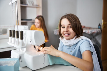 Cheerful girl using sewing machine in tailor studio