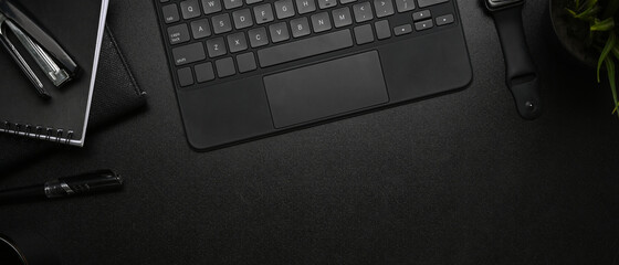 Horizontal image of modern dark workplace with smart watch, keyboard and notebook on black leather.