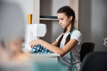 Adorable girl sewing fabric in dressmaking studio