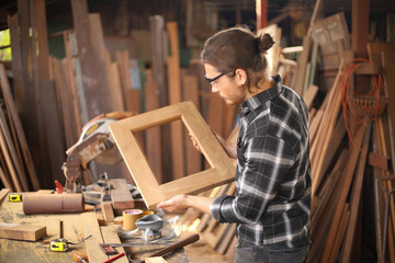 Young Caucasian carpenter man is making wooden frame in his own garage style workshop for hobby with copy space